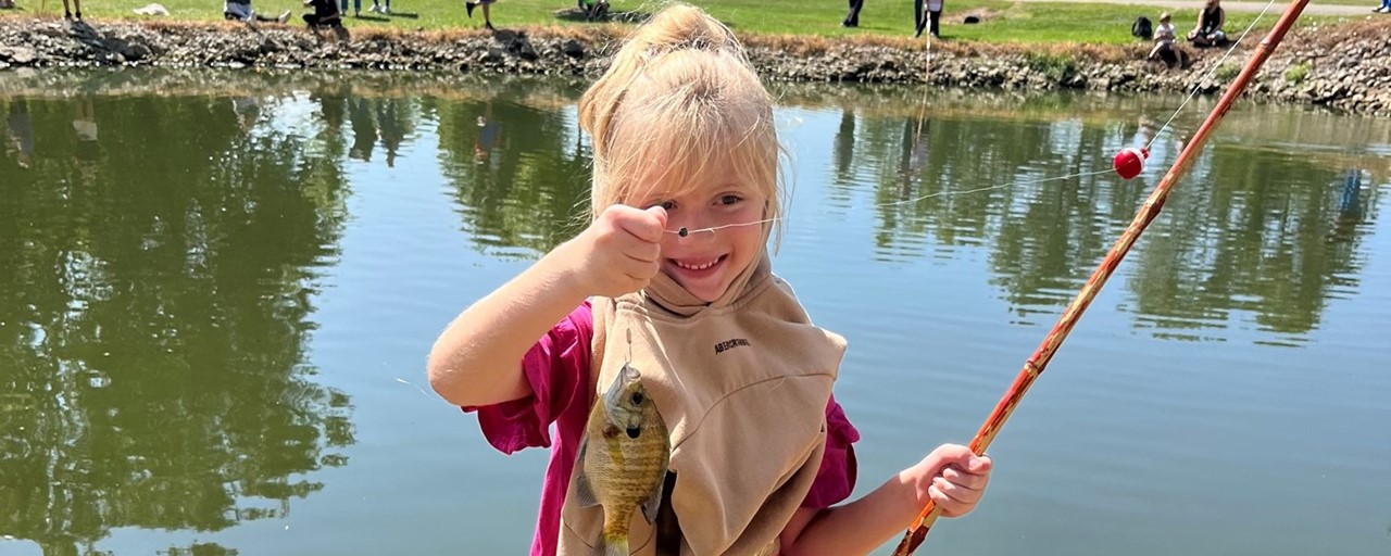 fishing day: little girl with blond hair holding a fish she caught and smiling.