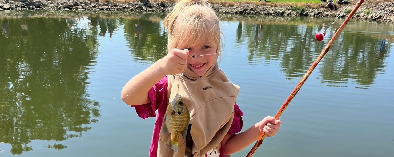fishing day: little girl with blond hair holding a fish she caught and smiling.